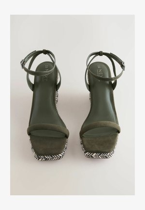 Olivengrønne højhælede sandaler med firkantede tæer, ankelremme og vævet sort-hvidt detaljer på sålen. Lavet af ruskind.