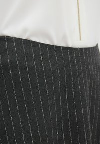 Gonna nera su misura con righe bianche, realizzata in tessuto strutturato. Presenta una parte superiore bianca liscia e una zip dorata.
