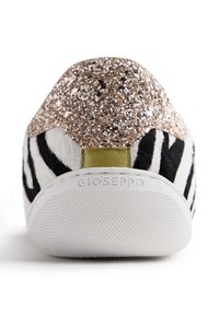 Baskets à imprimé zèbre avec un dessus texturé noir et blanc, talon en paillettes dorées et semelle en caoutchouc blanche, avec un petit accent vert.