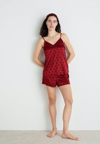 Set de pijamale din satin, de culoare mov, cu buline, format dintr-un top cu decolteu în V și pantaloni scurți asortați. Textură fină, bretele subțiri și design simplu.