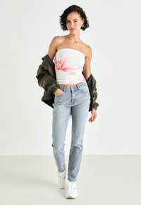 Uten skulderstropper blomstret topp med rosa accenter, lyse denimbukser og en mørk grønn bomberjakke. Hvite sneakers fullfører antrekket.