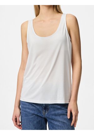 Kobieta w prostym białym bezrękawnym topie z okrągłym dekoltem i niebieskich dżinsach, stojąca na białym tle.