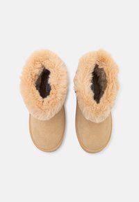 Smeđe ante slippers s mekim, pahuljastim bež oblogom. Dizajn s zaobljenim vrhom, ravni potplat i bez vidljivih metalnih dijelova ili ukrasa.