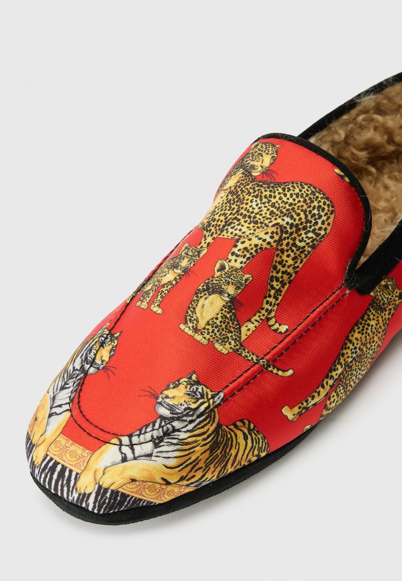 Rote Stoffschlupfschuhe mit einem gedruckten Design von Leoparden und Tigern, einem weichen Innenfutter und schwarzer Umrandung um die Sohle.