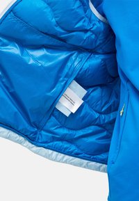 Blaues, isoliertes Jackeninnere mit glänzender Stoffstruktur, gestepptem Muster und einem Etikett mit Pflegeanweisungen. Mit Reißverschlusstasche.