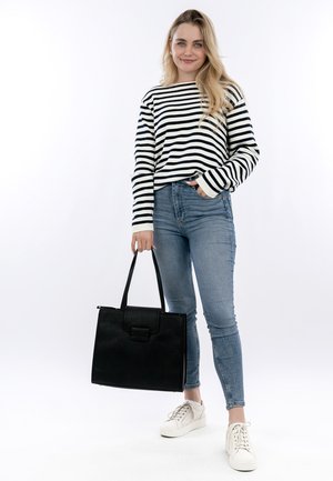 Black textured tote bag with top handles, worn with a striped long-sleeve shirt and blue jeans, paired with white sneakers.
