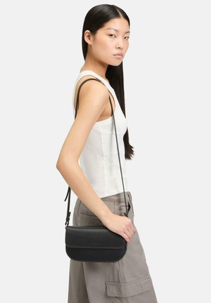 Czarna skórzana torba na ramię z klapką, cechująca się smukłym kształtem, eleganckim designem oraz regulowanym paskiem, noszona na ramieniu.