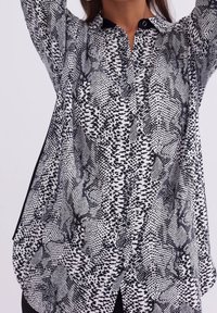 Black and white patterned button-up shirt with varied textures, featuring a collar and side slits for ease of movement.