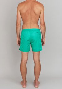Shorts de bain verts avec une taille élastique et des poches latérales, présentant une texture lisse et un minimalisme de la marque au dos.