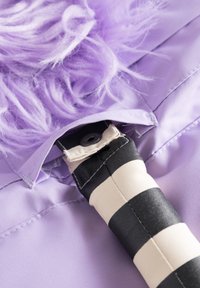 Lila tygaccessoar med fluffig textur, med ett randigt handtag i svart och kräm och en knapp-förslutning.