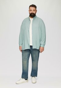 Lichtblauwe button-up shirt over een wit t-shirt, gecombineerd met blauwe jeans en witte sneakers. Glad materiaal, relaxte pasvorm, recht model.