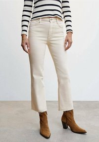 Jeans cortos de color beige claro con dobladillo deshilachado, combinados con botines de ante marrón con tacón. Un suéter a rayas en blanco y negro completa el conjunto.
