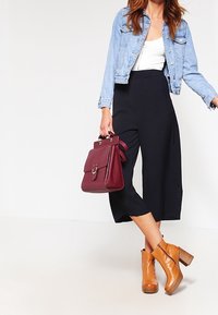 Chaqueta de mezclilla, blusa blanca, culottes negros, botas de tobillo marrones con tacones gruesos y un bolso burdeos con un detalle de hardware circular.