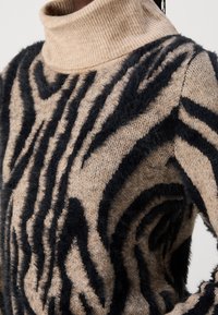 Beige polotröja med svarta strukturerade zebra ränder. Mjukt, fluffigt material ger djup; ribbad krage förbättrar både komfort och stil.