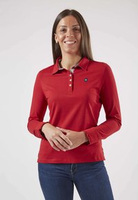 Polo-shirt rouge à manches longues avec un col, une patte de boutonnage et un col intérieur à motifs. Présente des poignets de manches à volants et un petit logo.