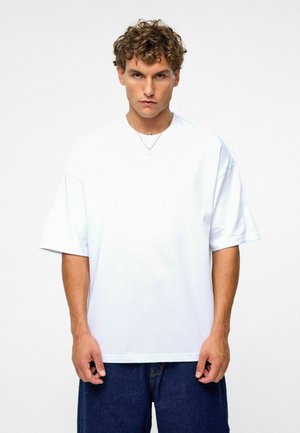 Witte oversized t-shirt van katoen, met korte mouwen en een ronde hals. Gecombineerd met donkerblauwe denimshorts.