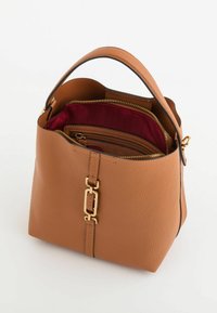 Tan lædertaske med en struktureret design, der har et håndtag og guldfarvet hardware. Indvendigt inkluderer den en lynlåslomme med burgunderfór.