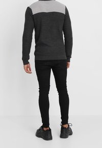 Pull pour homme en gris foncé avec une partie supérieure à motif gris clair. Design en tricot texturé, col rond, associé à un jean noir ajusté et des baskets noires.