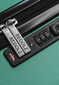 Maleta rígida con un exterior texturizado de color menta, que cuenta con dos tiradores de cremallera plateados etiquetados como "REDOLZ" y una cerradura de combinación con tres discos.