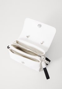 Hvid læderpung med lås. Den har to lynlåslommer og et stofbånd. Minimalistisk design med sølvhardware.