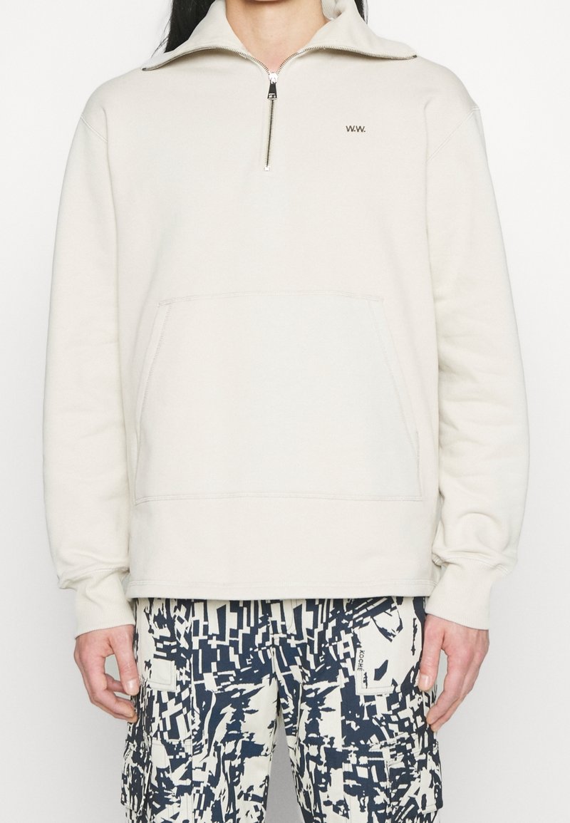 Světlé béžové mikina na zip s vysokým límcem, přední kapsou a vyšitým logem W.W. Měkká, texturovaná látka.