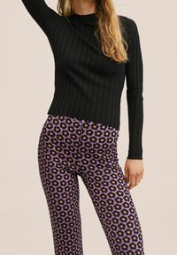 Czarny prążkowany top z długim rękawem w połączeniu z fioletowymi legginsami z kwiatowym wzorem w czerni i pomarańczy.