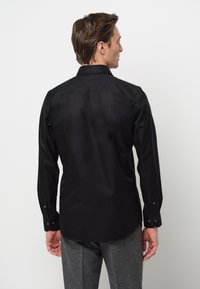 Maglietta nera a maniche lunghe con colletto strutturato, texture liscia e polsini con bottoni, mostrata da dietro su uno sfondo bianco.