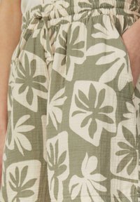 Shorts en tissu à motifs floraux verts avec une taille élastique, un cordon de serrage et des poches latérales ; fabriqués à partir d'un matériau léger et texturé.