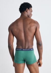 Bóxer de algodón verde con una cinturilla de marca en azul marino, diseño ajustado, textura suave y sin patrones visibles.