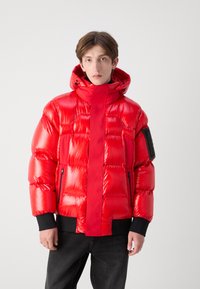 Rød pufferjakke med en skinnende, quilted tekstur, høj krave og en aftagelig hætte. Har sorte detaljer og sidelommer med lynlås.