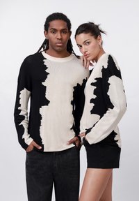 Jerséis de punto en negro y crema con patrones abstractos. La tela tiene una textura suave. Uno se combina con pantalones oscuros, el otro con pantalones cortos.
