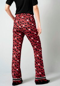 Rode broek met patronen en zwart-witte abstracte vormen. Heeft een rechte pijp, zakken en zwarte afwerking aan de zoom.