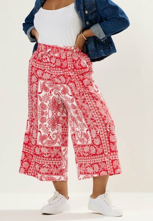 Kvinde iført bredbenede, cropped bukser med røde og hvide blomstrede paisley-mønstre, hvide sneakers, hvid top og denimjakke.