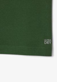 Vihreä puuvillakangas, jossa on sileä pinta ja oikeassa alareunassa harmaa "ULTRA DRY" -labeli. Yksinkertainen saumurisauma.