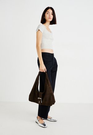 Chemise grise raccourcie, pantalon sombre et ballerines argentées métalliques. Tenant un sac marron foncé texturé avec une boucle argentée. Design simple et matériaux doux.