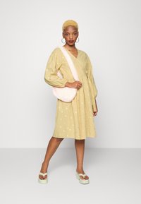 Vestido amarelo floral com mangas balão, decote em V e saia em camadas; bolsa de ombro felpuda rosa; sandálias de plataforma verdes.