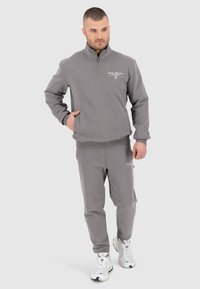 Pull en polaire gris avec un zip quart et un logo brodé, associé à un pantalon de survêtements fuselé assorti. Comprend des poignets et une taille à bords côtelés.