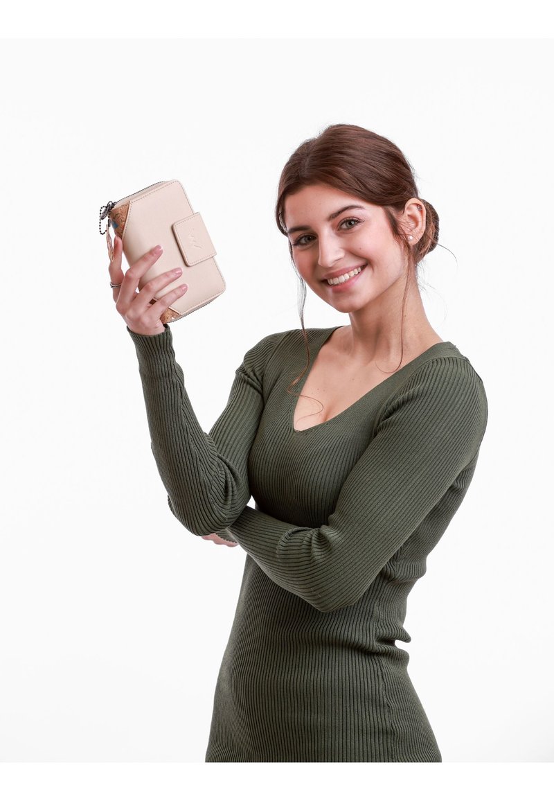 Beige wallet with a textured surface and a clasp, held by a model in a fitted olive green ribbed dress against a white background.