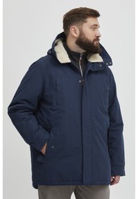 Mørkeblå jakke med hette foret med fuskepels, frontglidelås og sidelommer. Den har rett snitt og er litt polstret.