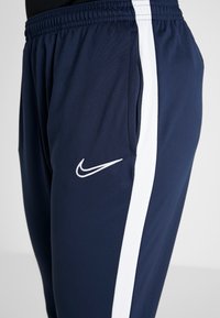 Marina atletiska byxor med vita sidostråk, elastisk midja och sidofickor. Har en liten vit Nike-logotyp ovanför vänster ficka.