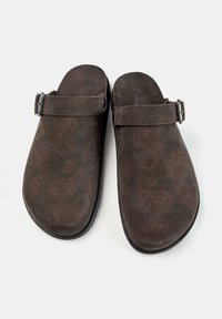 Brązowe zamszowe klompy z wzorem paisley, z regulowanym metalowym klamrem, solidnymi czarnymi podeszwami i otwartym tyłem dla łatwego zakupu.