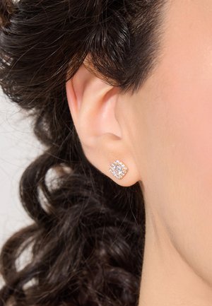 Różowe złote kolczyki wkrętki z kwadratowym wzorem, z centralnym okrągłym kamieniem otoczonym mniejszymi, przezroczystymi kamieniami. Gładkie wykończenie metalowe.