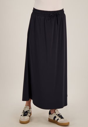 Zwarte lange rok met elastische tailleband en trekkoord, gedragen met witte sneakers met zwarte strepen en rubberen zolen.