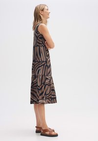 Brown tiered dress with abstract black and white pattern, sleeveless design, and relaxed fit, paired with brown strappy sandals.