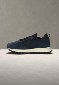 Baskets bleu foncé en tissu texturé avec semelle en caoutchouc, avec lacets à l'avant, logo sur le côté et languette à l'arrière du talon.