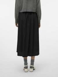 Gonna nera midi con pieghe, maglione grigio corto, calzini grigi e scarpe platform off-white. Tessuto liscio, design semplice, minimi dettagli.