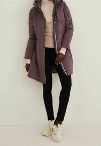 Fioletowa wodoodporna kurtka parka z kapturem, z guzikami z przodu i kieszeniami po bokach. Nosi się ją na lekkim swetrze, a w zestawieniu z czarnymi legginsami i białymi trampkami.