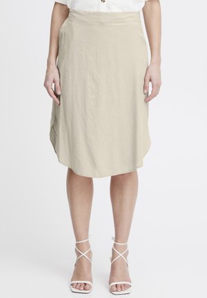 Beige, knee-length skirt made of lightweight fabric with a slight sheen. Features a high waist and curved hem. Paired with white strappy heels.