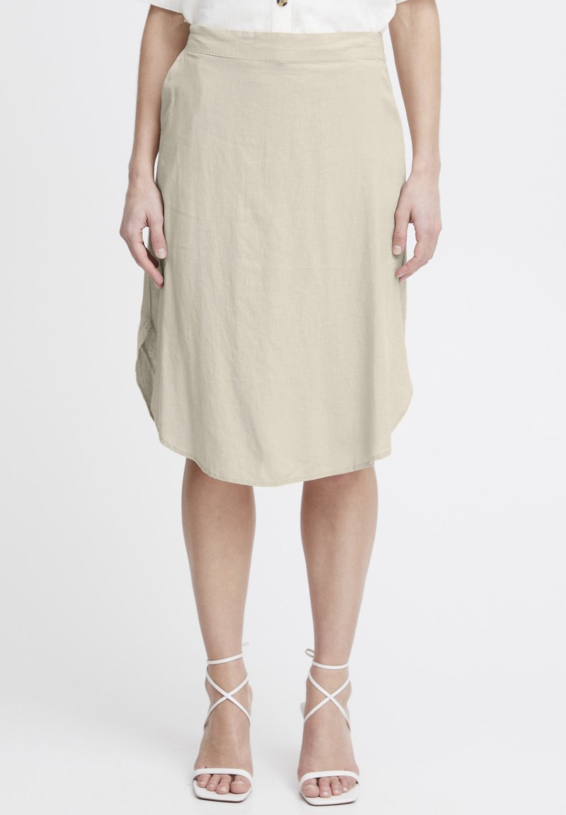 Jupe beige, hauteur genou, en tissu léger avec un léger éclat. Elle présente une taille haute et un ourlet arrondi. Associée à des talons blancs à lanières.