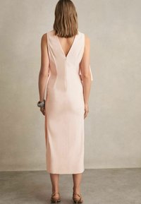 Rochie de un roz pal, fără mâneci, cu decolteu în V și slituri laterale, confecționată dintr-un material moale, având un fermoar ascuns și un design minimalist.